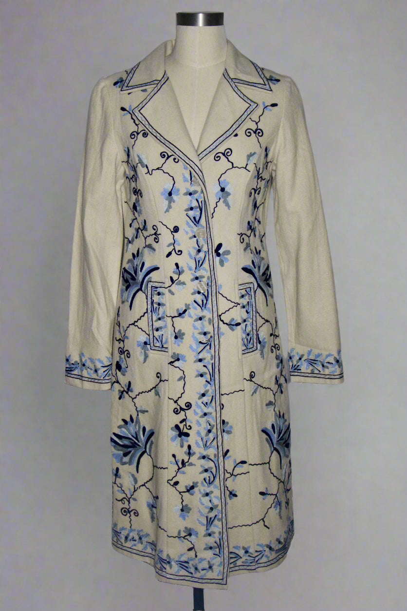 Beige coat with blue floral embroidery on a mannequin against a gray background