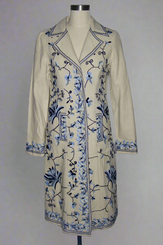 Beige coat with blue floral embroidery on a mannequin against a gray background