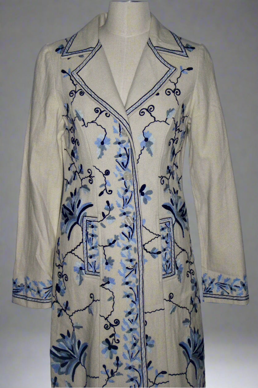 Beige coat with blue floral embroidery on a mannequin against a gray background